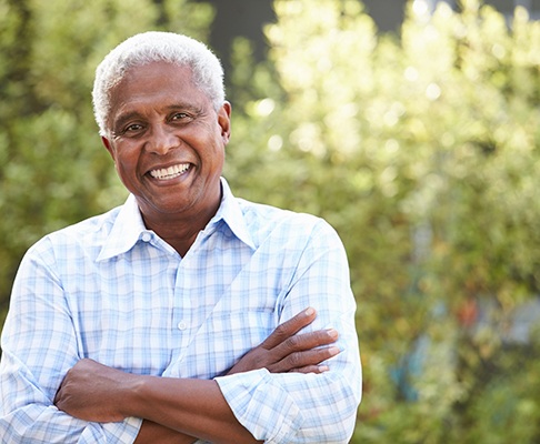 Senior man standing outside smiling with arms folded